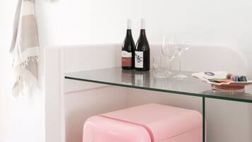 Een roze, vintage koelkast met een glazen blad, twee flessen wijn en twee wijnglazen op een witte tafel.