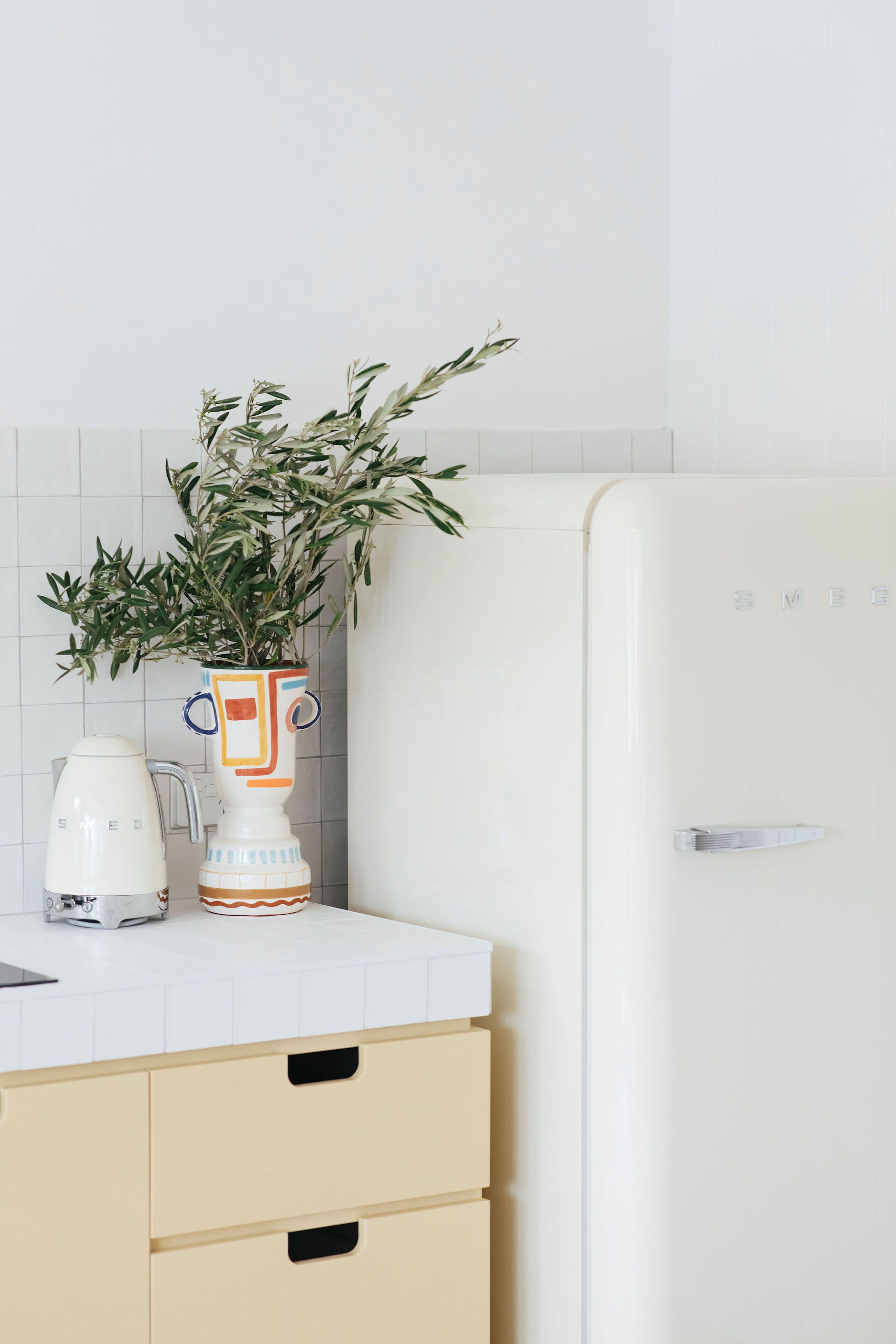 A kitchen with a white refrigerator, a white coffee maker, and a vase with a plant on the counter.
