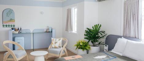 Ein Hotelzimmer mit Bett, zwei Stühlen, einem kleinen Tisch, einer Zimmerpflanze und einer Küchenzeile.