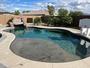 A swimming pool with a curved design, a small waterfall feature, and a basketball hoop. - Beautiful home with Heated Pool, Outdoor Bar, Spring Training, Golf (Buckeye)