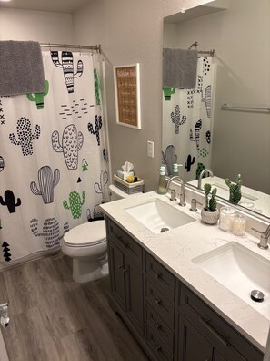 A bathroom with a white sink, two mirrors, a toilet, and a shower curtain with cactus designs. - Beautiful home with Heated Pool, Outdoor Bar, Spring Training, Golf (Buckeye)