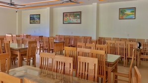 A dining area with wooden chairs and tables, ceiling fans, and framed artwork on the walls. - Khach san So Oanh  (Dam Thuy)