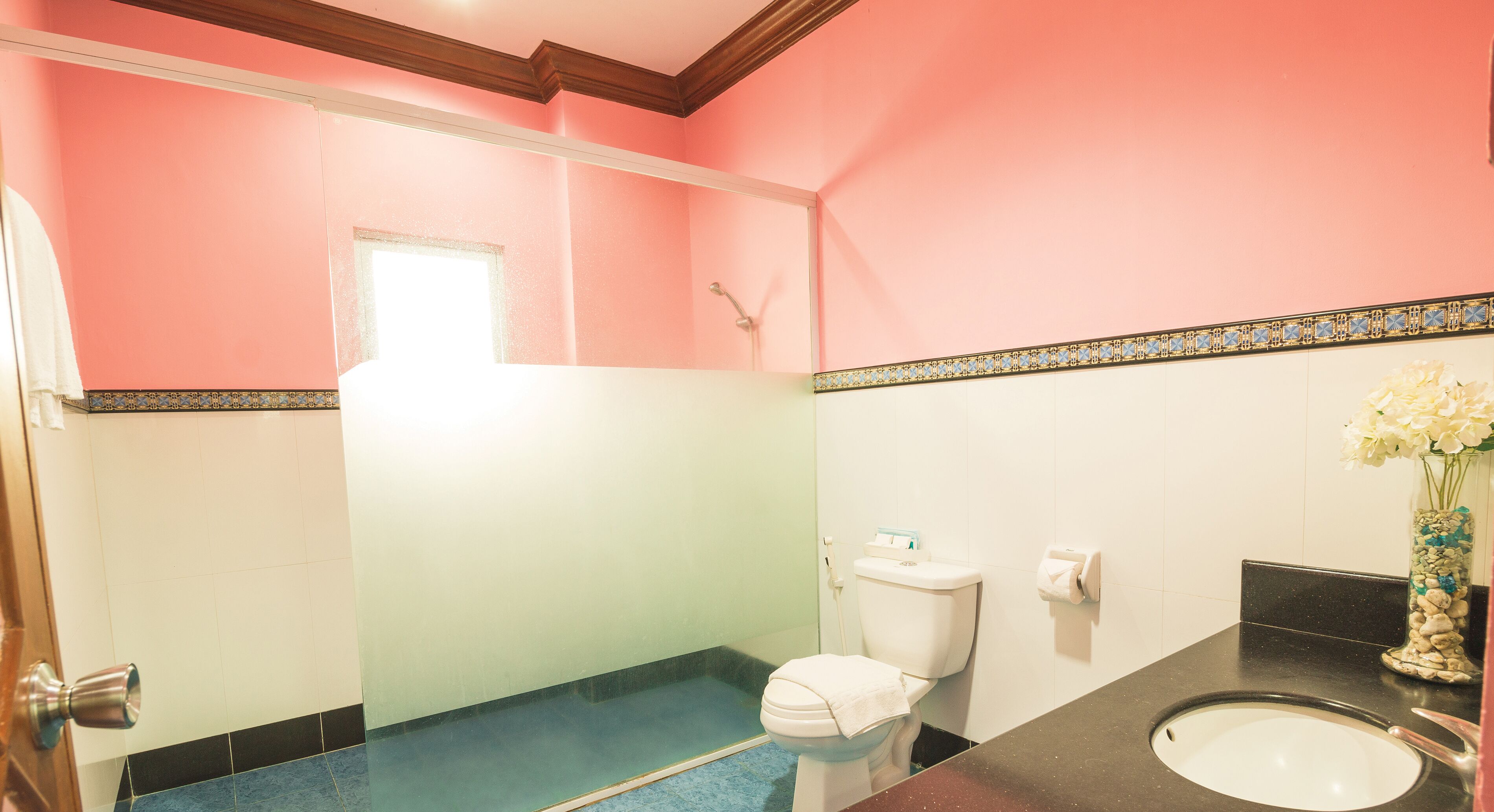 A bathroom with a pink wall, a white toilet, a sink, and a shower.