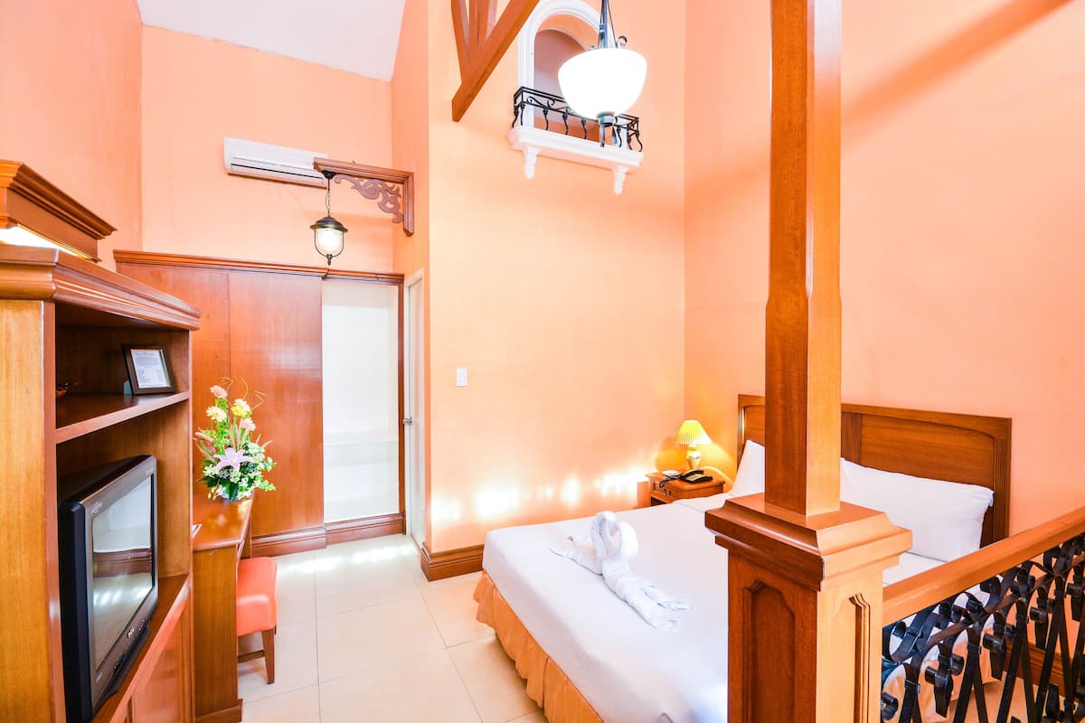 Une chambre d’hôtel avec un lit en bois, une télévision, un bureau avec une lampe et un petit tabouret.