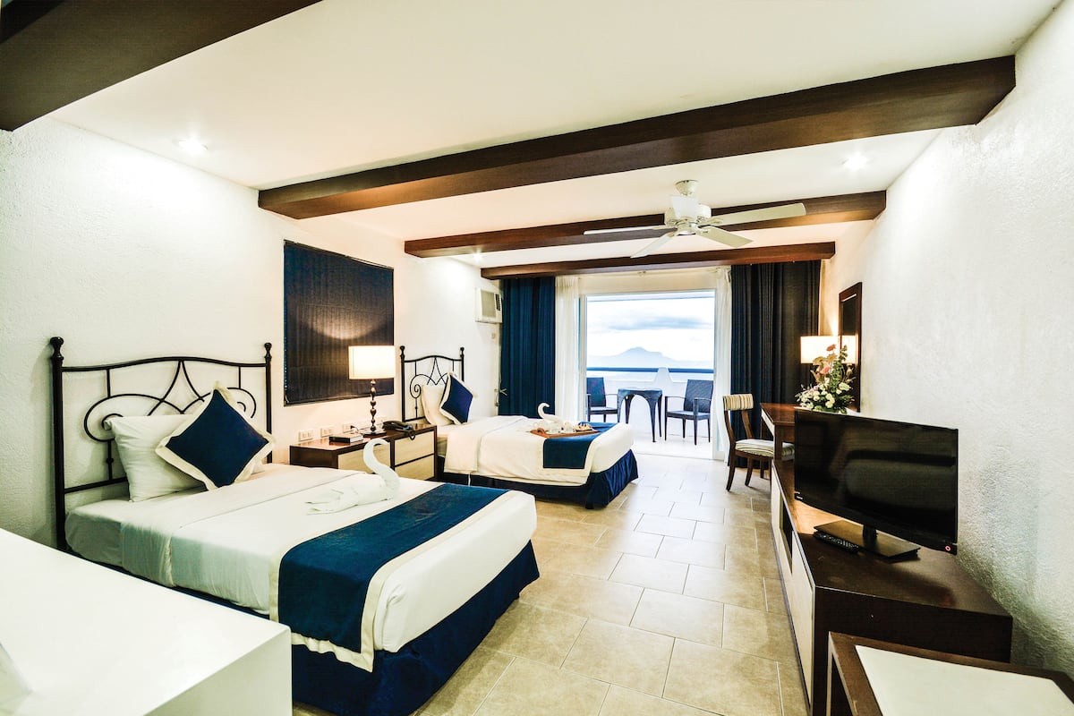 Une chambre d’hôtel avec deux lits, une télévision, un bureau et une vue sur la mer.