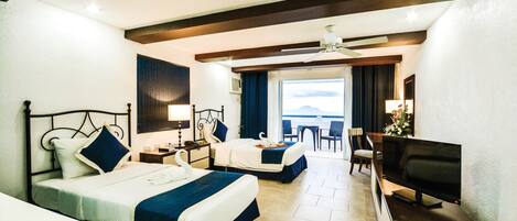 Habitación de hotel con dos camas, televisión, escritorio y vista al mar.