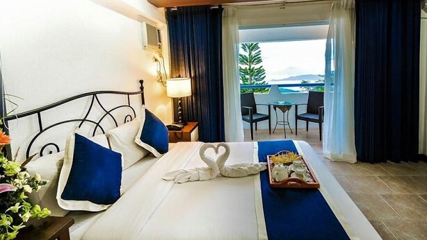 A hotel room with a bed, a tray with breakfast items, a balcony with a table and chairs, and a view of the sea. - Estancia Resort Hotel (Tagaytay)