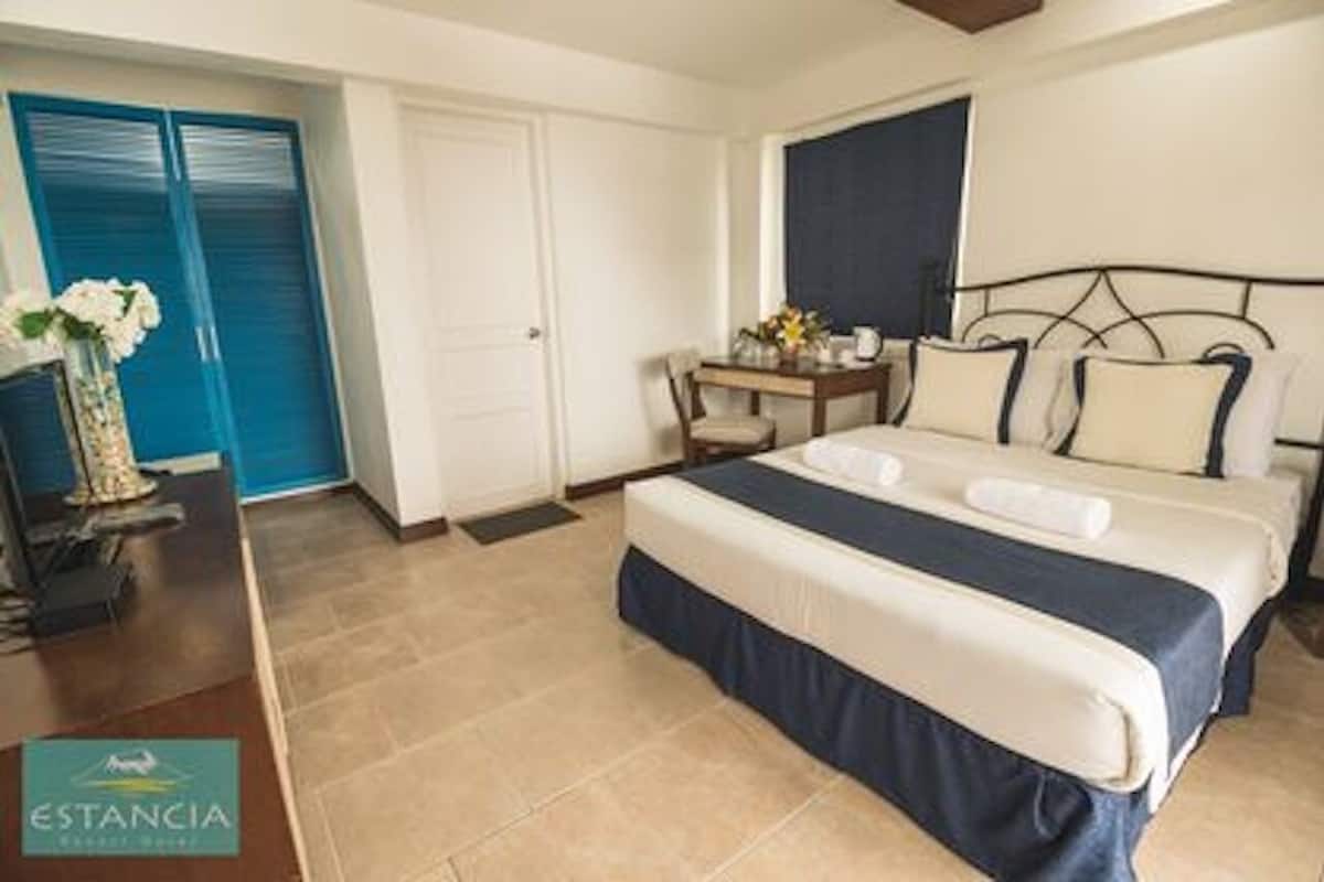 Une chambre d’hôtel avec un lit, un bureau et une chaise, un vase avec des fleurs et une porte bleue.