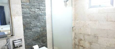 Un baño con pared de piedra, cabina de ducha de vidrio, inodoro y lavabo.