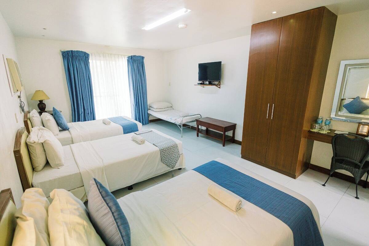 Une chambre d’hôtel avec deux lits, un bureau, une chaise, une télévision et une armoire.