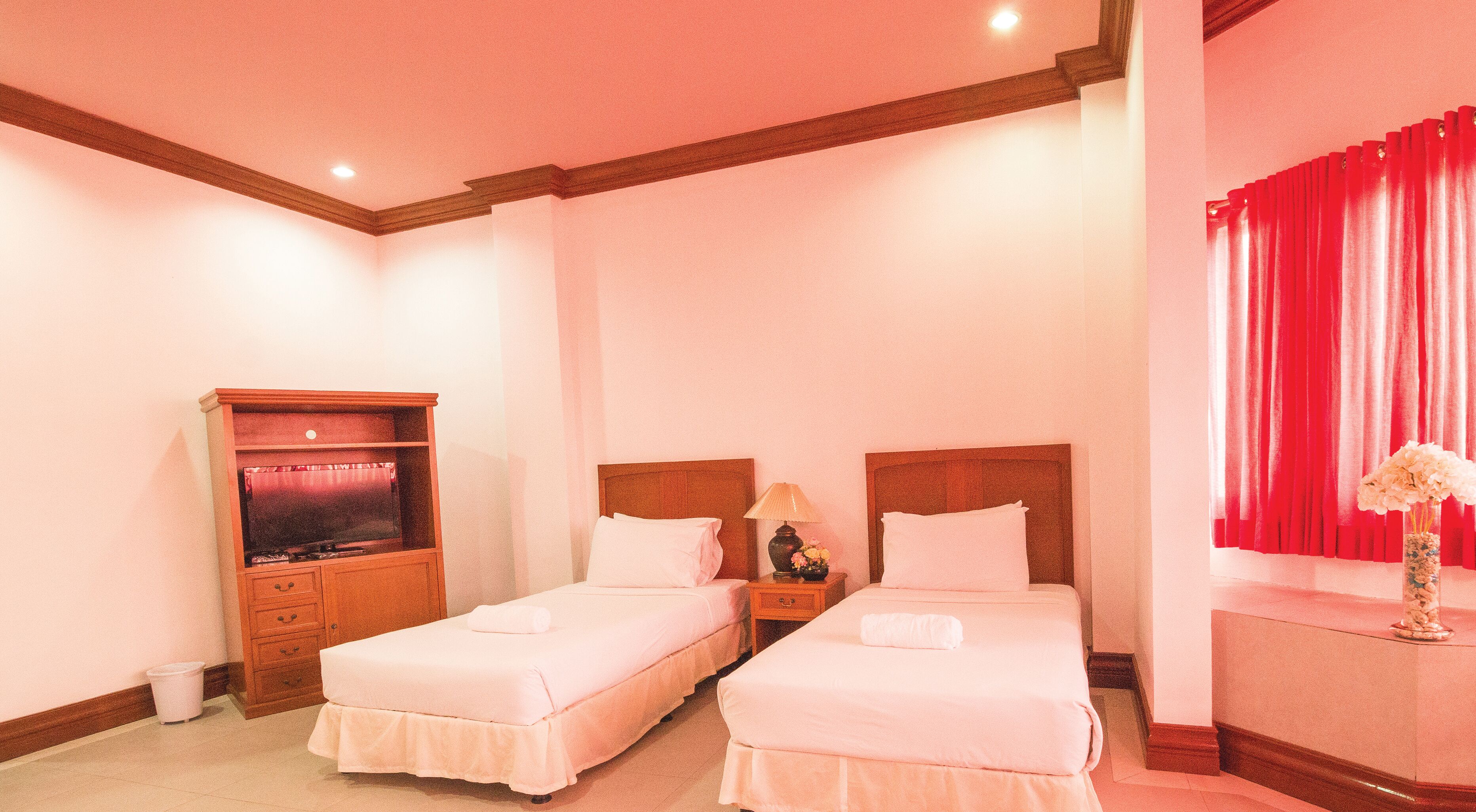 A hotel room with two beds, a television, a nightstand, and a red curtain.