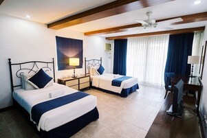 Habitación de hotel con dos camas, un escritorio, televisión y ventilador de techo.