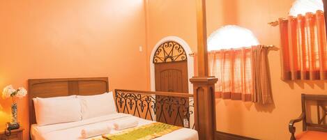 A hotel room with a wooden four-poster bed, a nightstand with a lamp, and a chair.