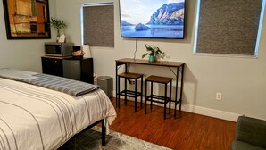 A bedroom with a bed, a desk with two stools, a TV on the wall, and a painting. - King. Minutes to Wilton Drive. Private entrance and bathroom. (Wilton Manors)
