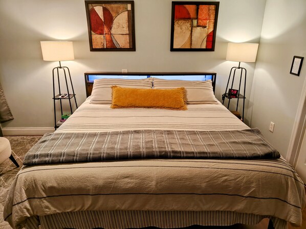 A neatly made bed with striped bedding, two wall-mounted abstract paintings, and bedside lamps.