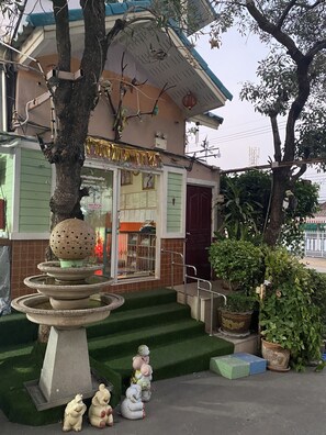 A building with a green facade, a small fountain with a decorative sphere, and a staircase leading to the entrance.