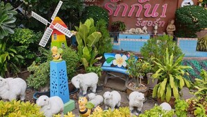 A garden with a windmill, sheep sculptures, and a bench with a flower design. - Ruckunresort 1 (Nakhon Sawan)