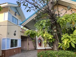 Un edificio con fachada de tejas, un extintor en la pared y un árbol de hojas verdes al frente.