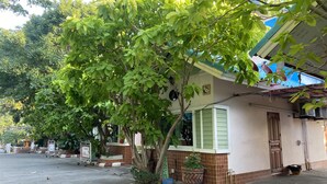 A residential street with a house featuring a tiled facade, a green door, and a potted plant in front. - Ruckunresort 1 (Nakhon Sawan)