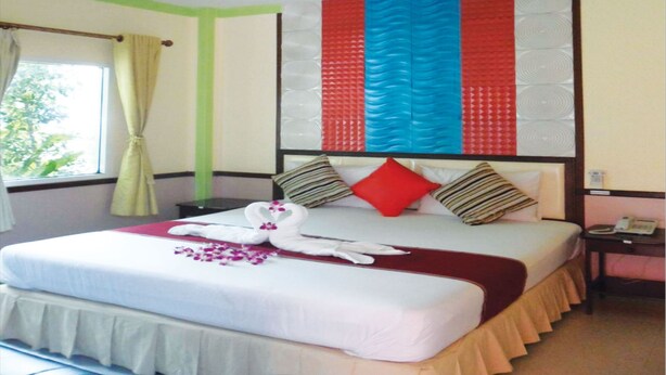 A hotel room with a bed, a nightstand, a telephone, and a window with curtains. - Ruckunresort 1 (Nakhon Sawan)