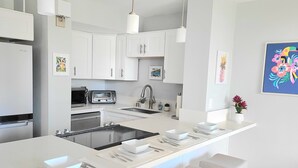 Une cuisine moderne avec des meubles blancs, un îlot central doté de sièges, un four à micro-ondes et un évier.