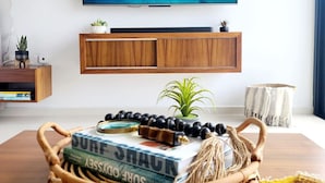 Sala de estar con una televisión mostrando una playa tropical, una mesa consola de madera con libros y una cesta tejida, y una planta pequeña sobre la consola.