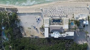 Vista aérea de un hotel costero con zona de playa, varias piscinas y aparcamiento.
