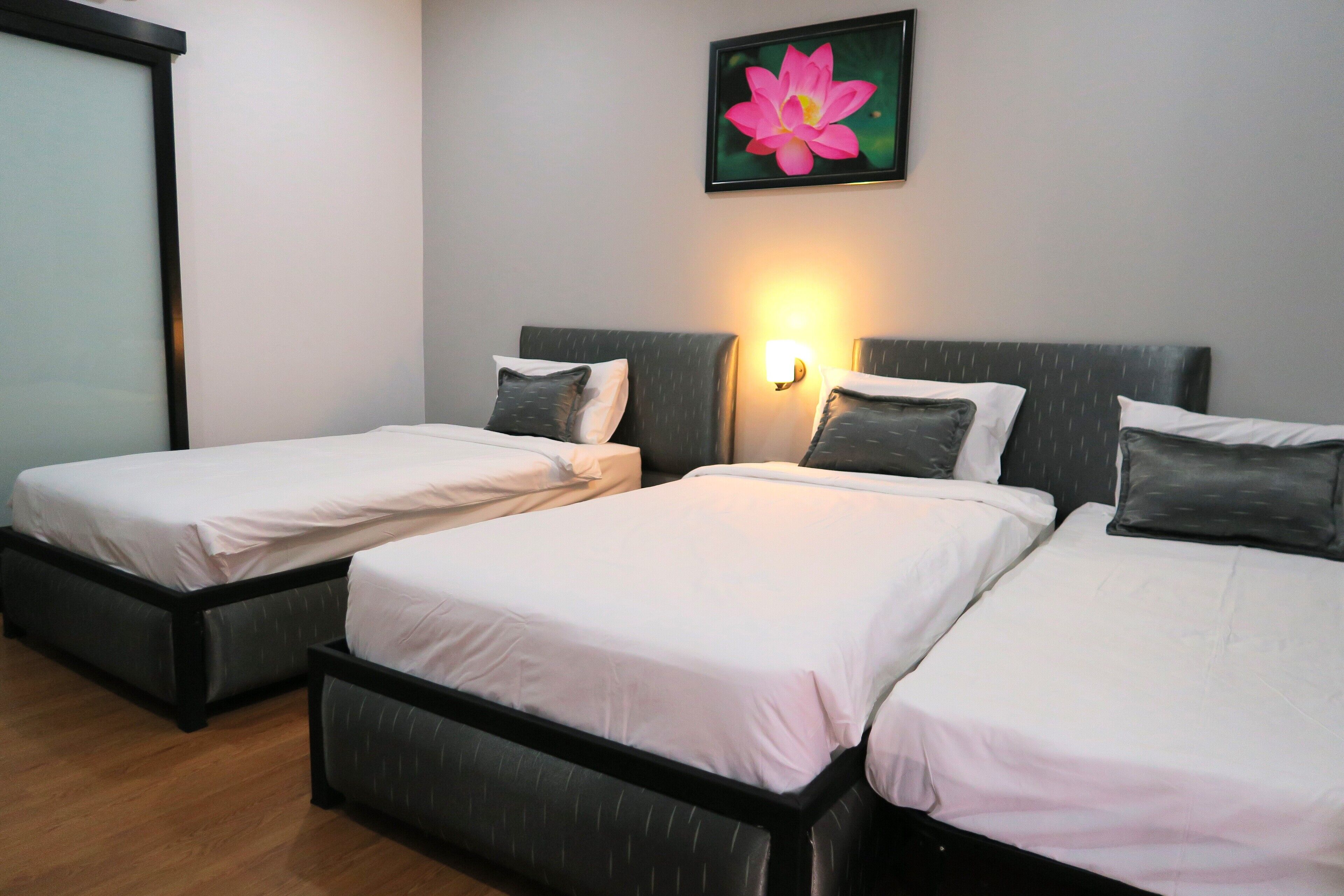 Habitación de hotel con dos camas individuales, cada una con almohada y cabecero. Hay una lámpara de pared sobre las camas y un cuadro con una flor en la pared.