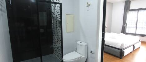 A modern bathroom with a glass shower enclosure, a white toilet, and a wooden floor.