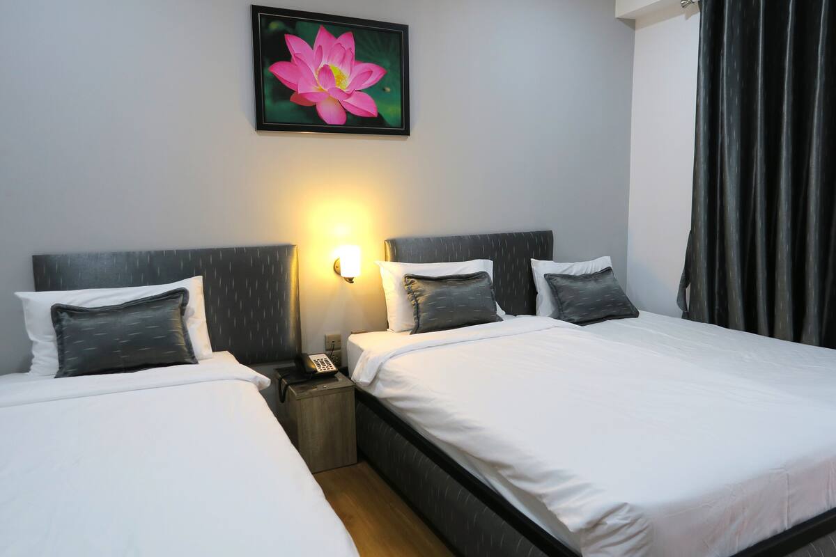 A hotel room with two beds, a nightstand with a phone, and a wall-mounted light.
