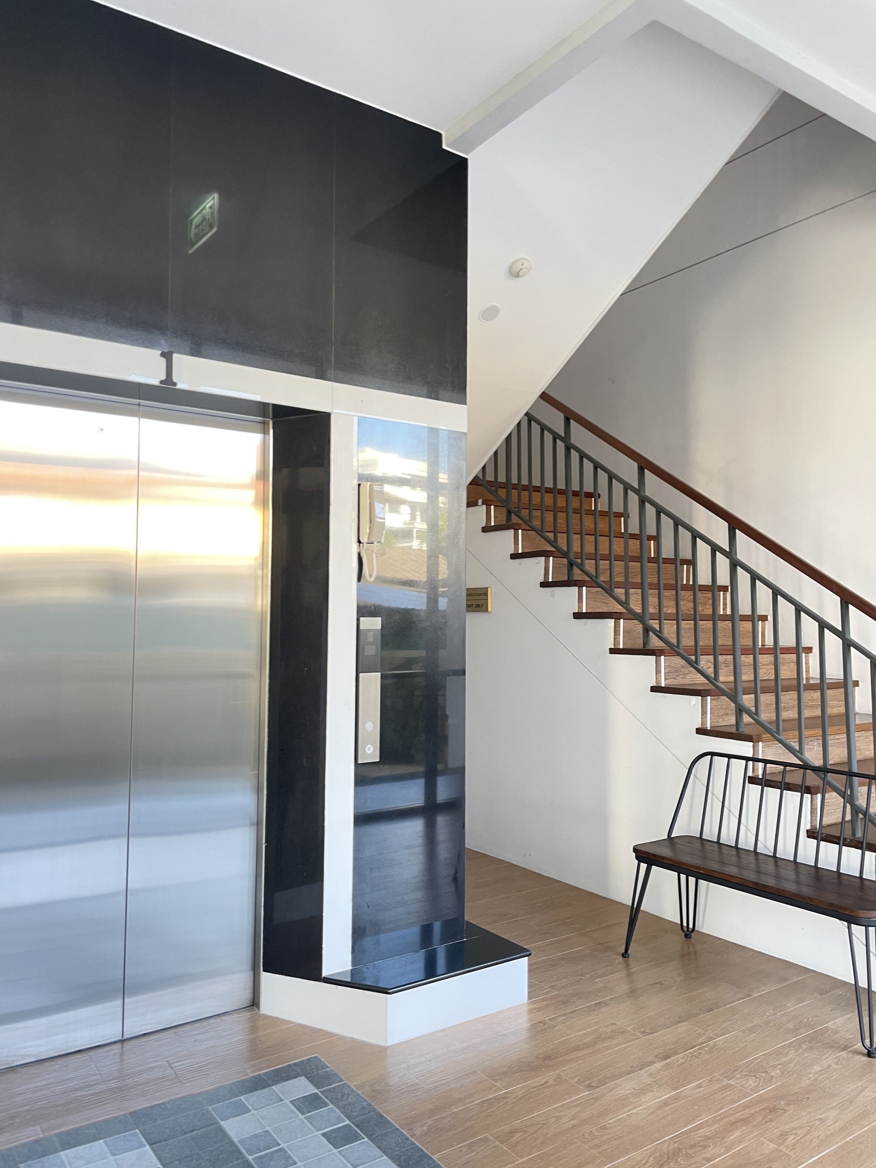 Un interior moderno con una escalera, un ascensor metálico y un suelo de madera.