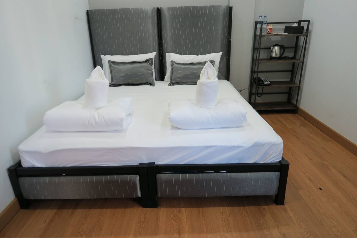A double bed with a grey headboard, two pillows, and a bedside table with a kettle and a bottle.
