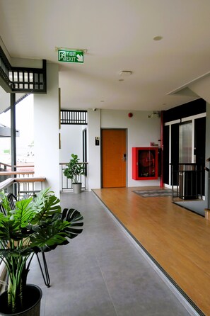 A modern hotel lobby with a wooden floor, a staircase, a red cabinet, and a potted plant.
