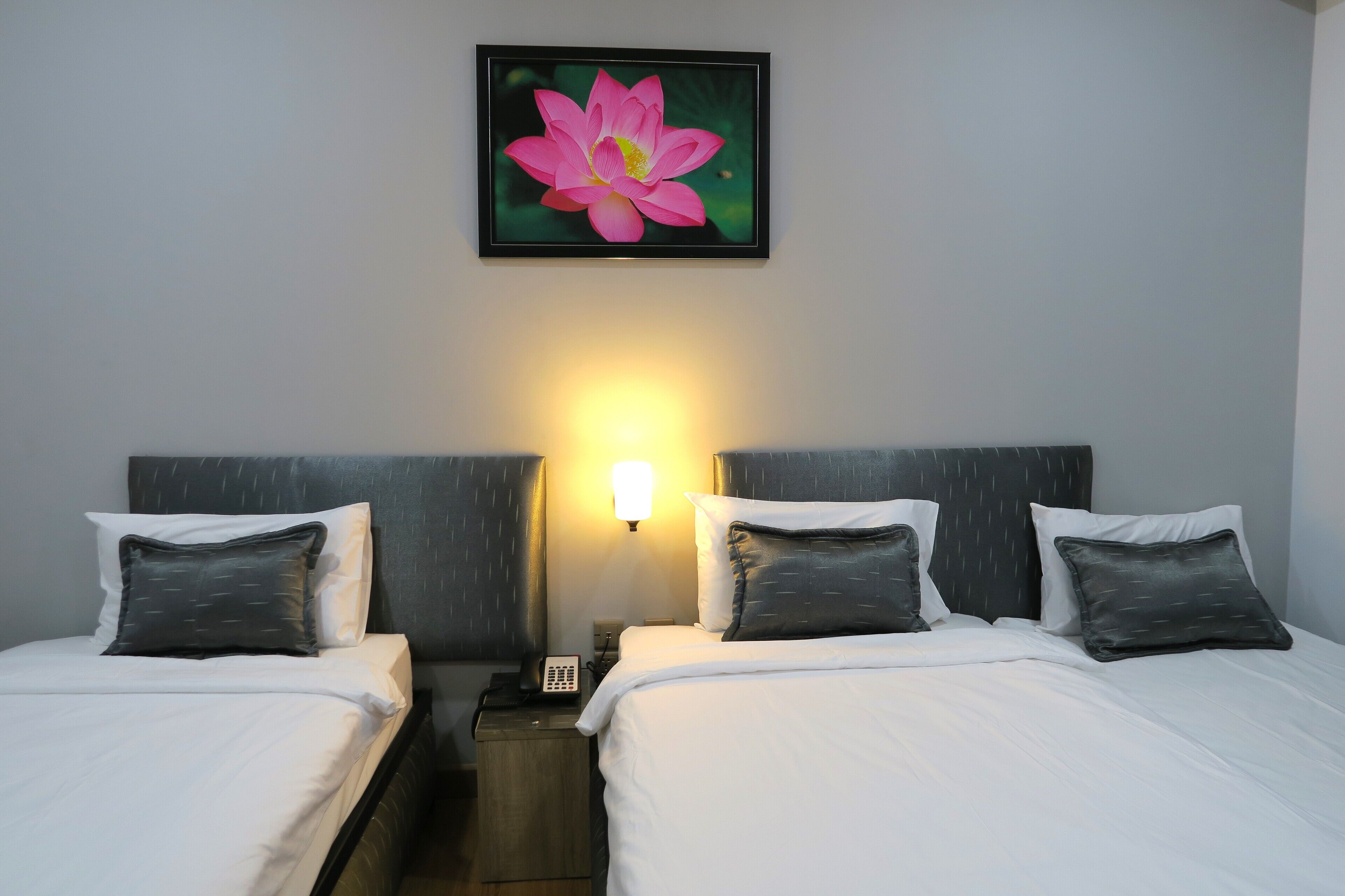 Habitación de hotel con dos camas, una mesita de noche con teléfono y una lámpara fijada a la pared.