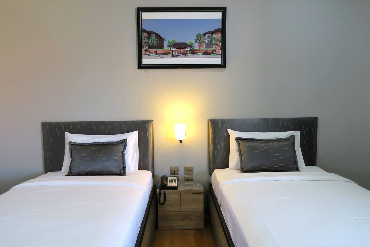 A hotel room with two beds, a nightstand with a phone, and a framed picture on the wall.