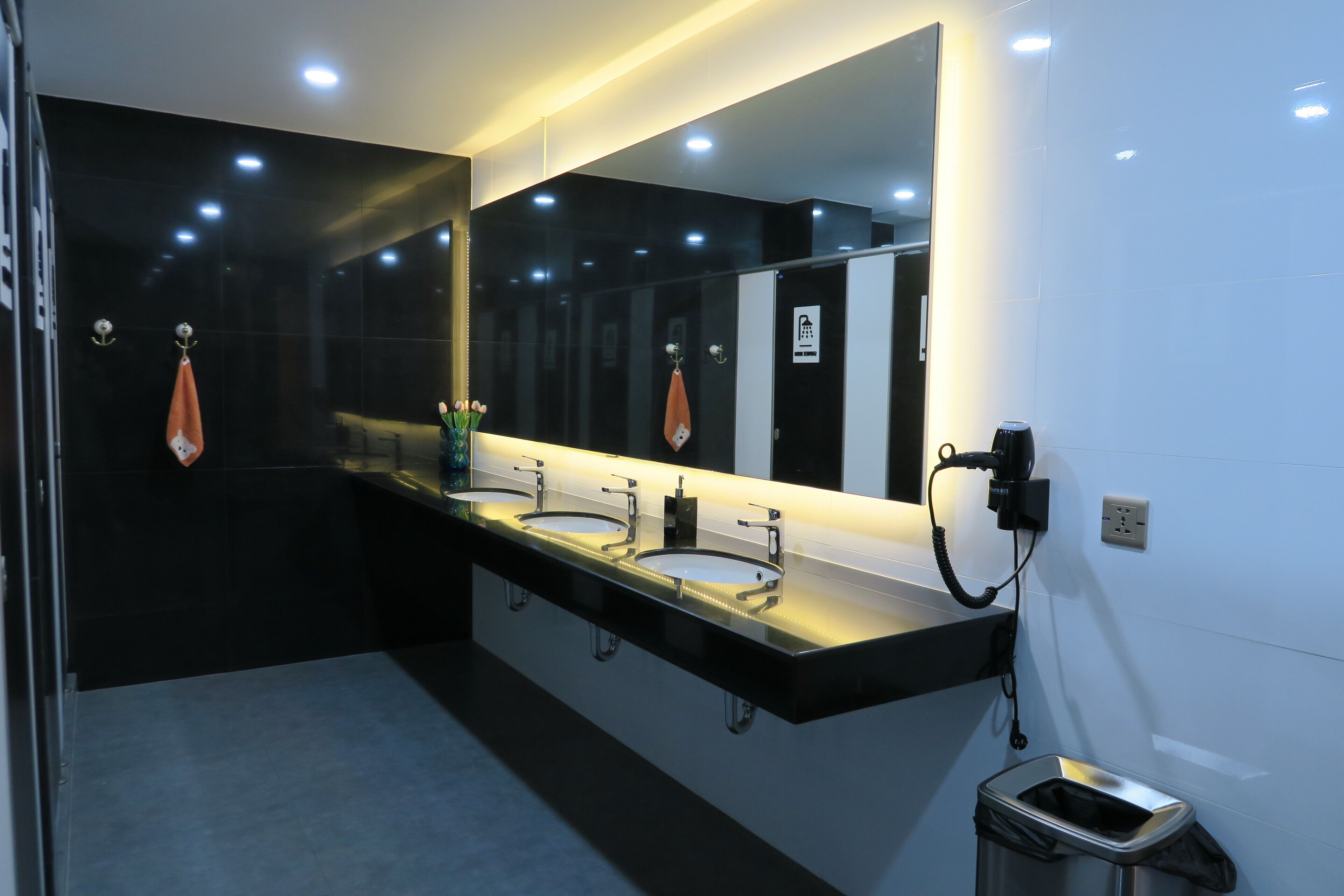 Une salle de bain moderne avec trois lavabos, un grand miroir et une poubelle.