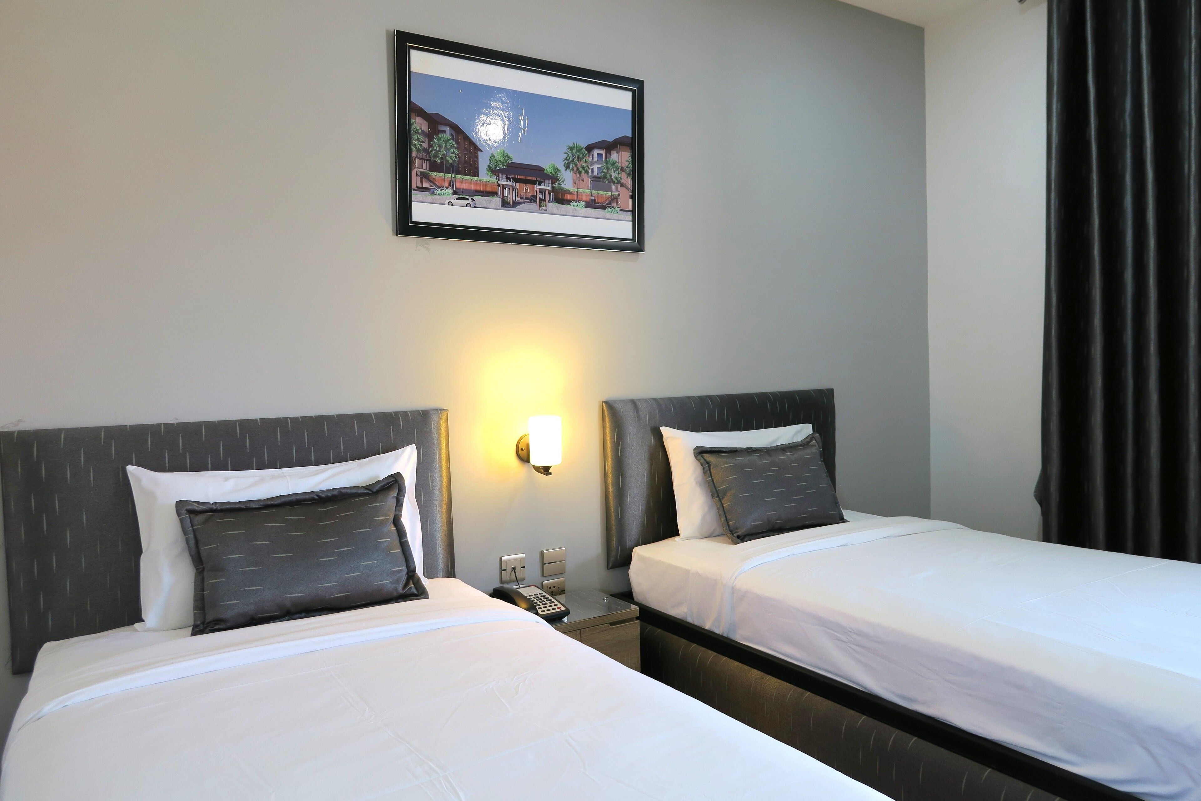 A hotel room with two beds, a nightstand with a phone, and a wall-mounted light.