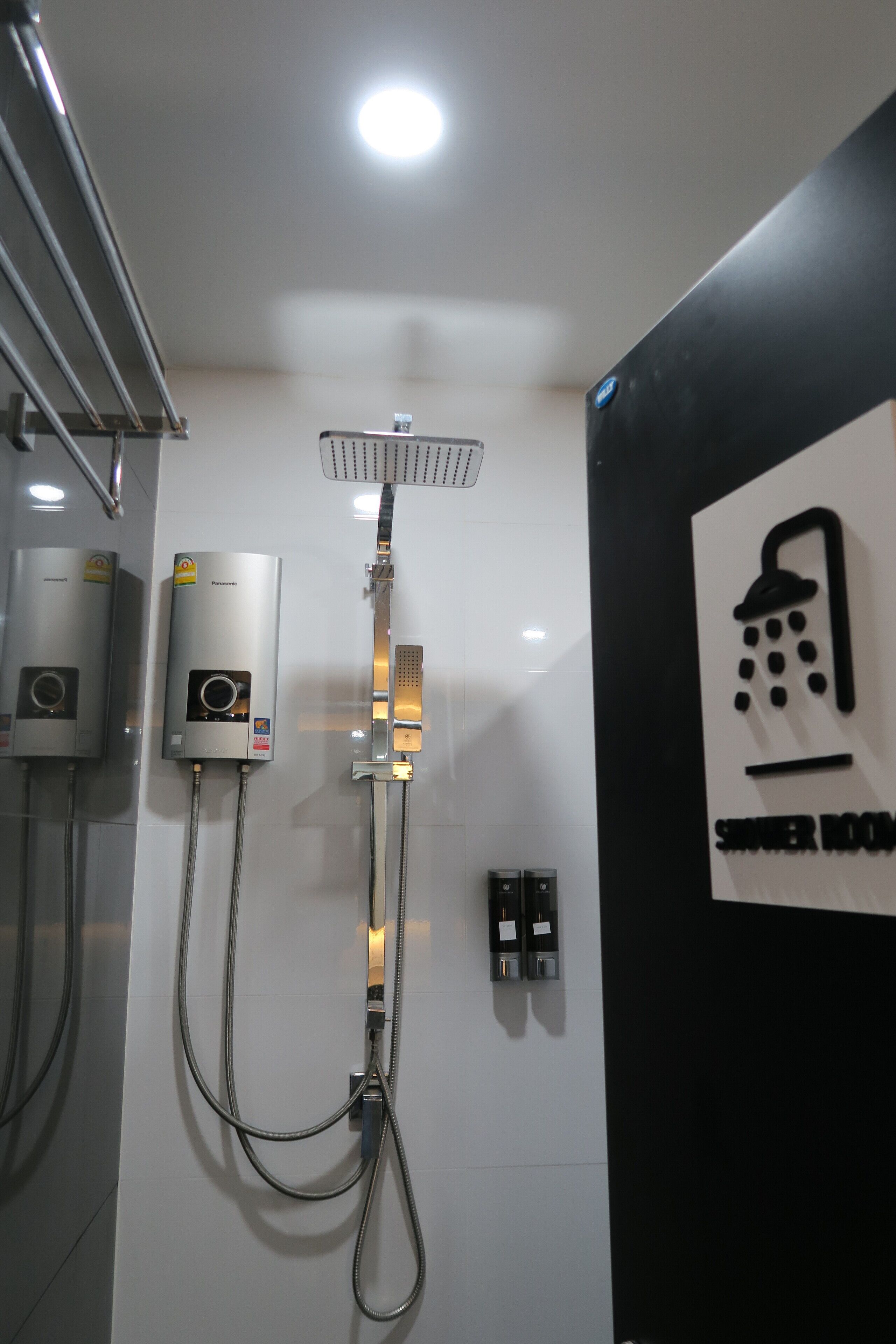 Baño con cabezal de ducha empotrado, ducha de mano y dos calentadores de agua en la pared.