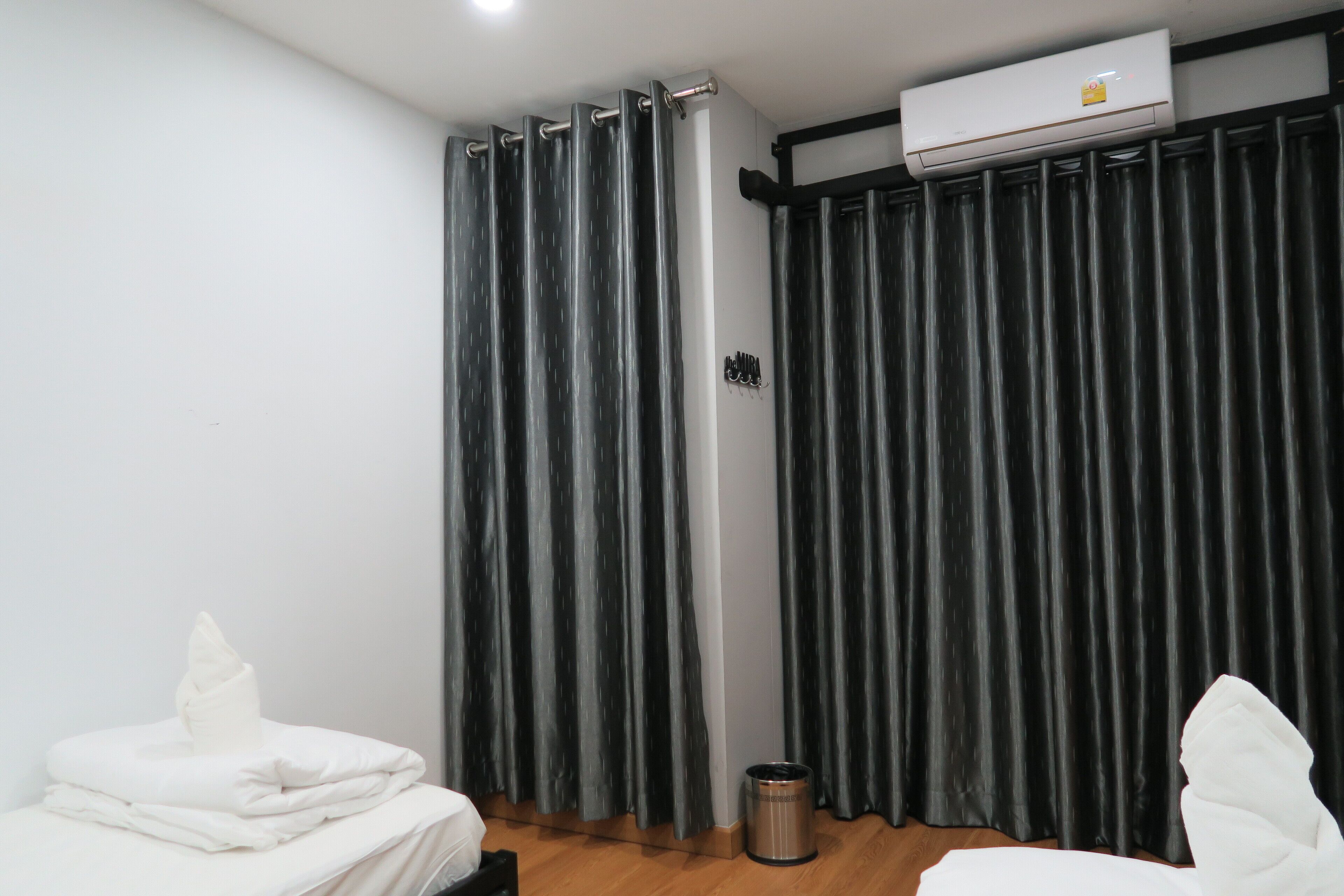 A hotel room with a bed, a small trash bin, and a window with curtains.