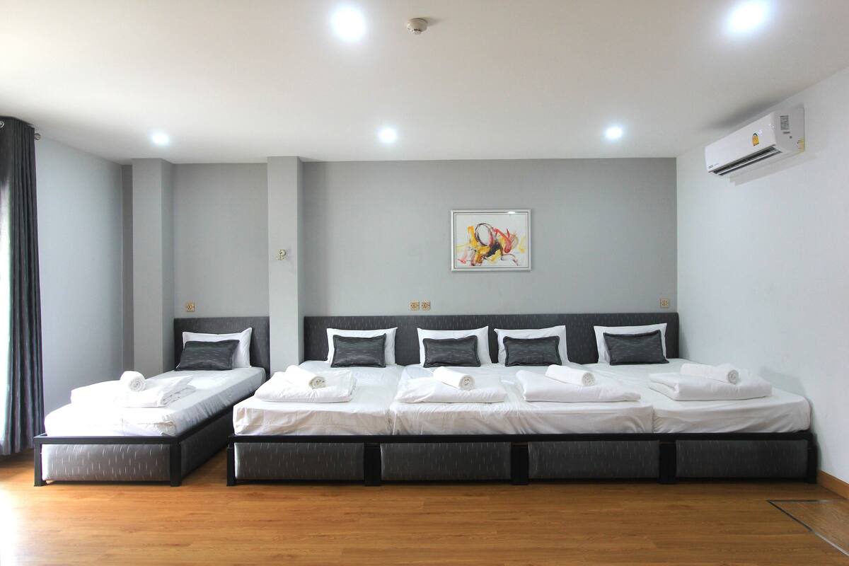 A hotel room with a large bed, two smaller beds, a ceiling fan, an air conditioning unit, and a painting on the wall.