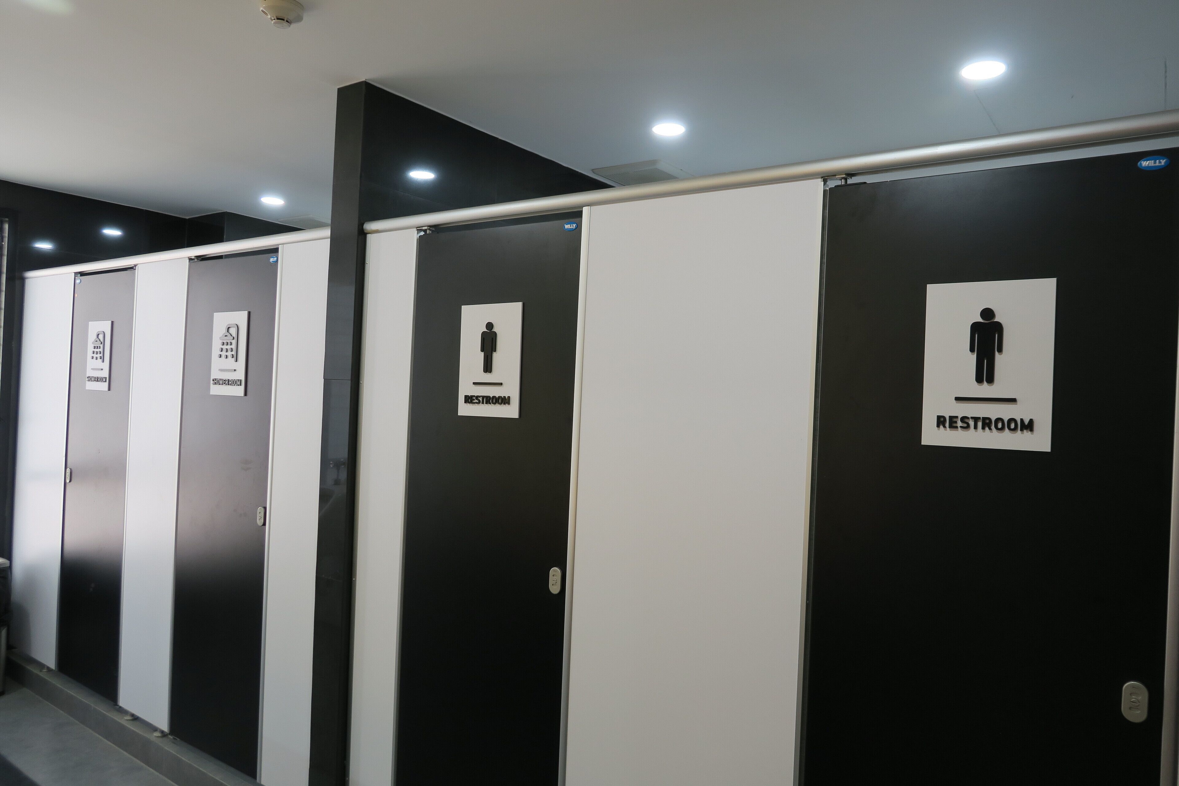 Une rangée de portes de toilettes noires et blanches, avec une pancarte indiquant qu’il s’agit des toilettes pour hommes.