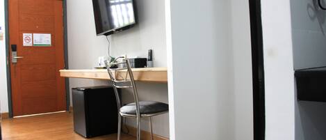 Una habitación con un escritorio de madera, una silla, un televisor montado en la pared y una puerta con un cartel.