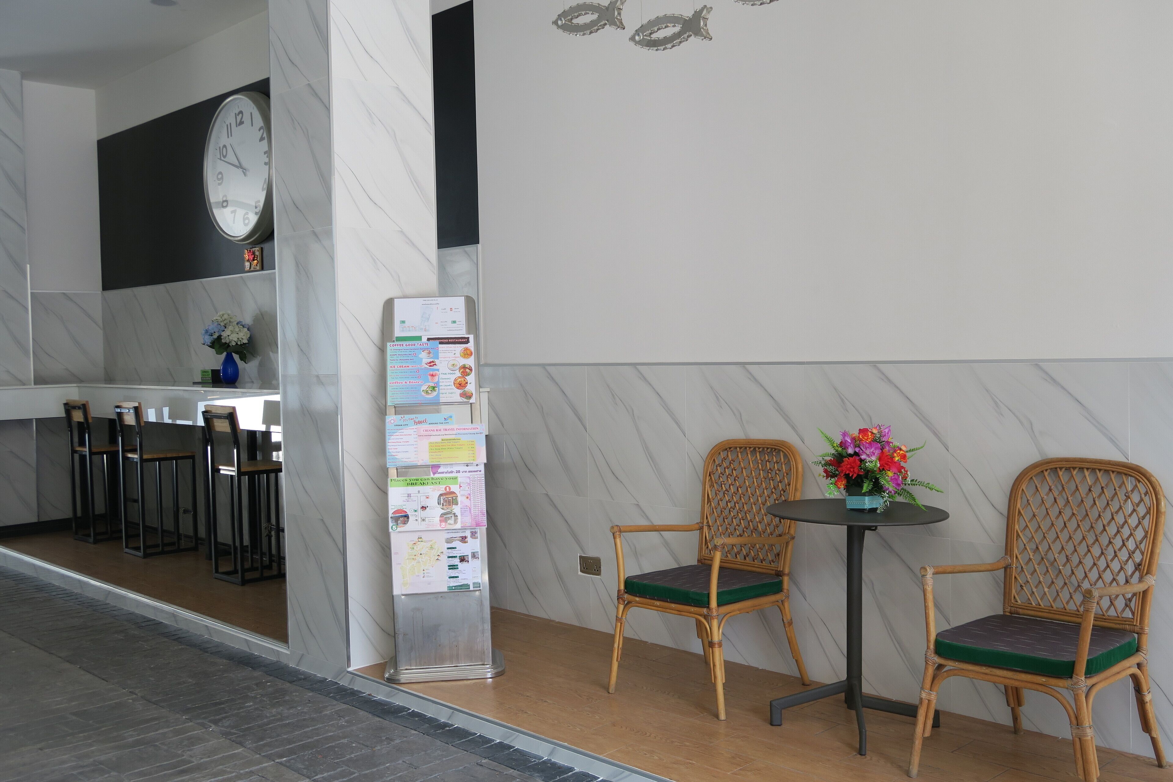 A modern interior with a marble wall, a clock, a refrigerator with various notices, and two wicker chairs with a small table.