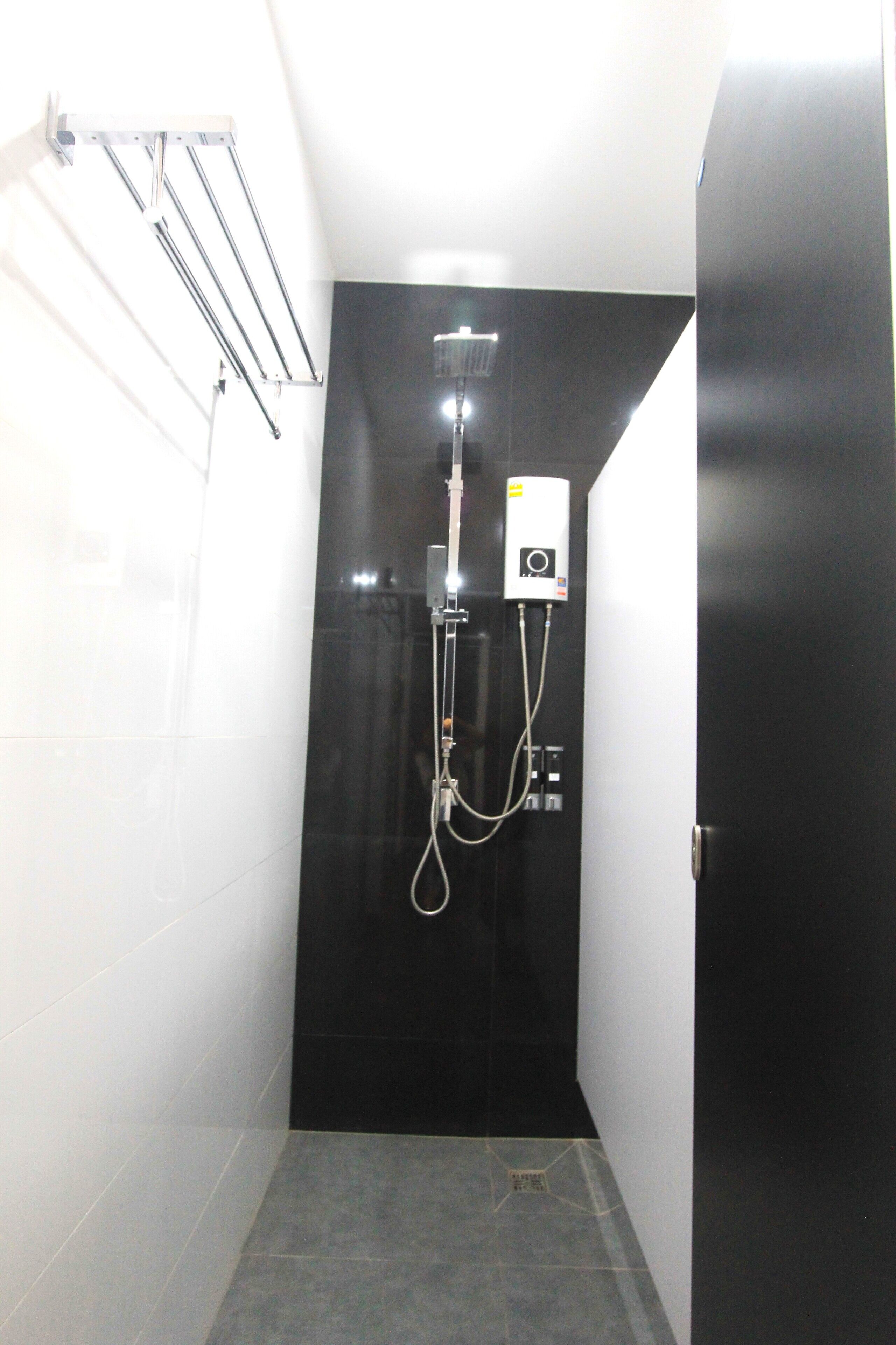 Une petite salle de bain moderne avec un mur recouvert de carreaux noirs, une douche avec un pommeau de douche amovible et un porte-serviettes fixé au mur.