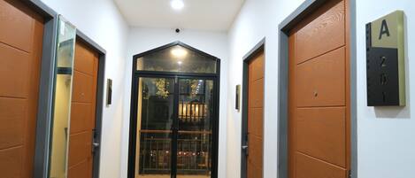 A hallway with two wooden doors, a black-framed glass door, and a wall-mounted sign with the letter 'A'.