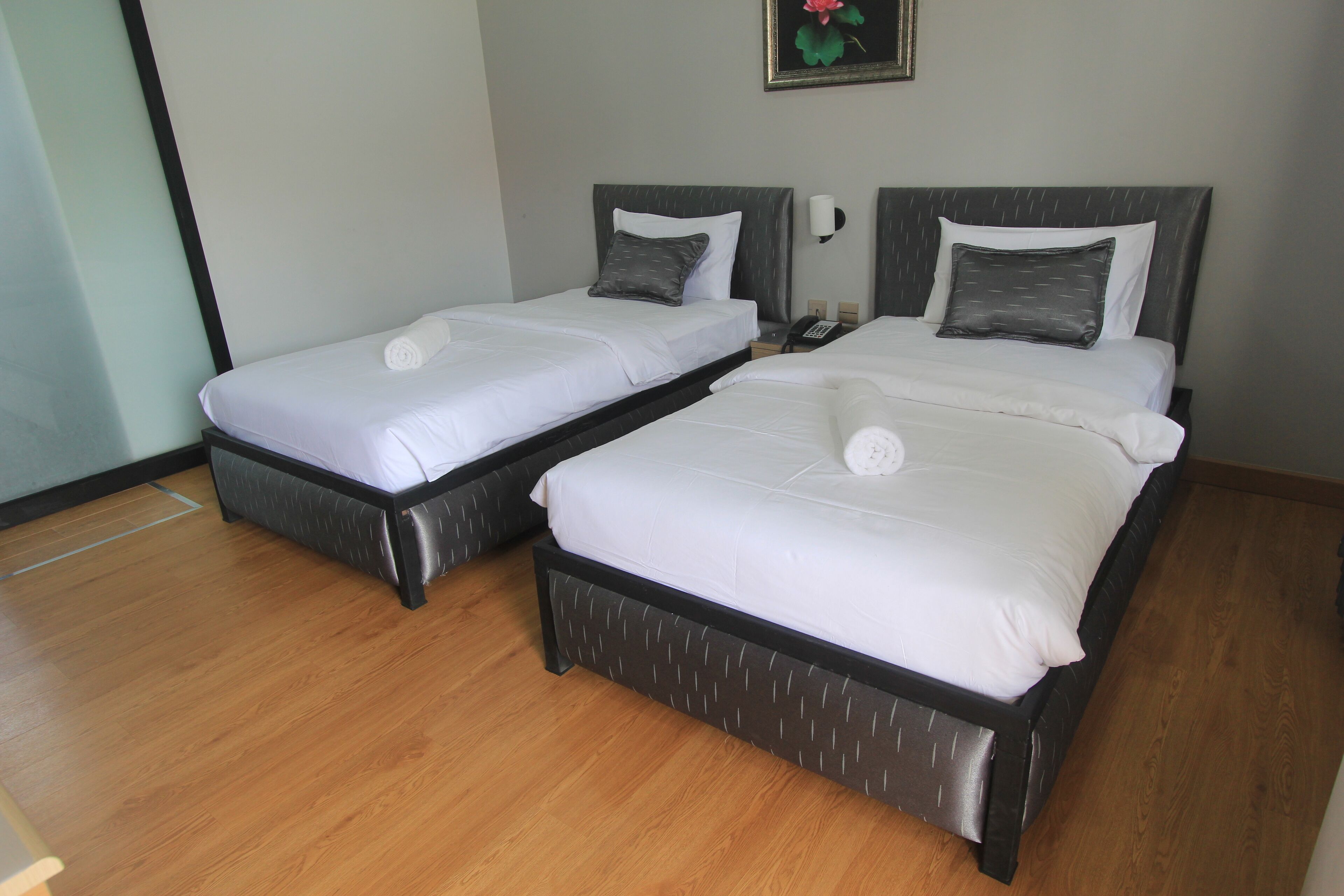 Deux lits simples avec des cadres sombres et du linge de lit blanc, un plancher en bois et un téléphone fixé au mur.