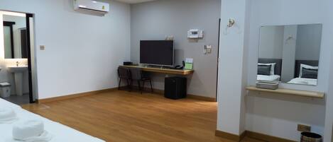 Una habitación de hotel con cama, escritorio, computadora, televisor y espejo.