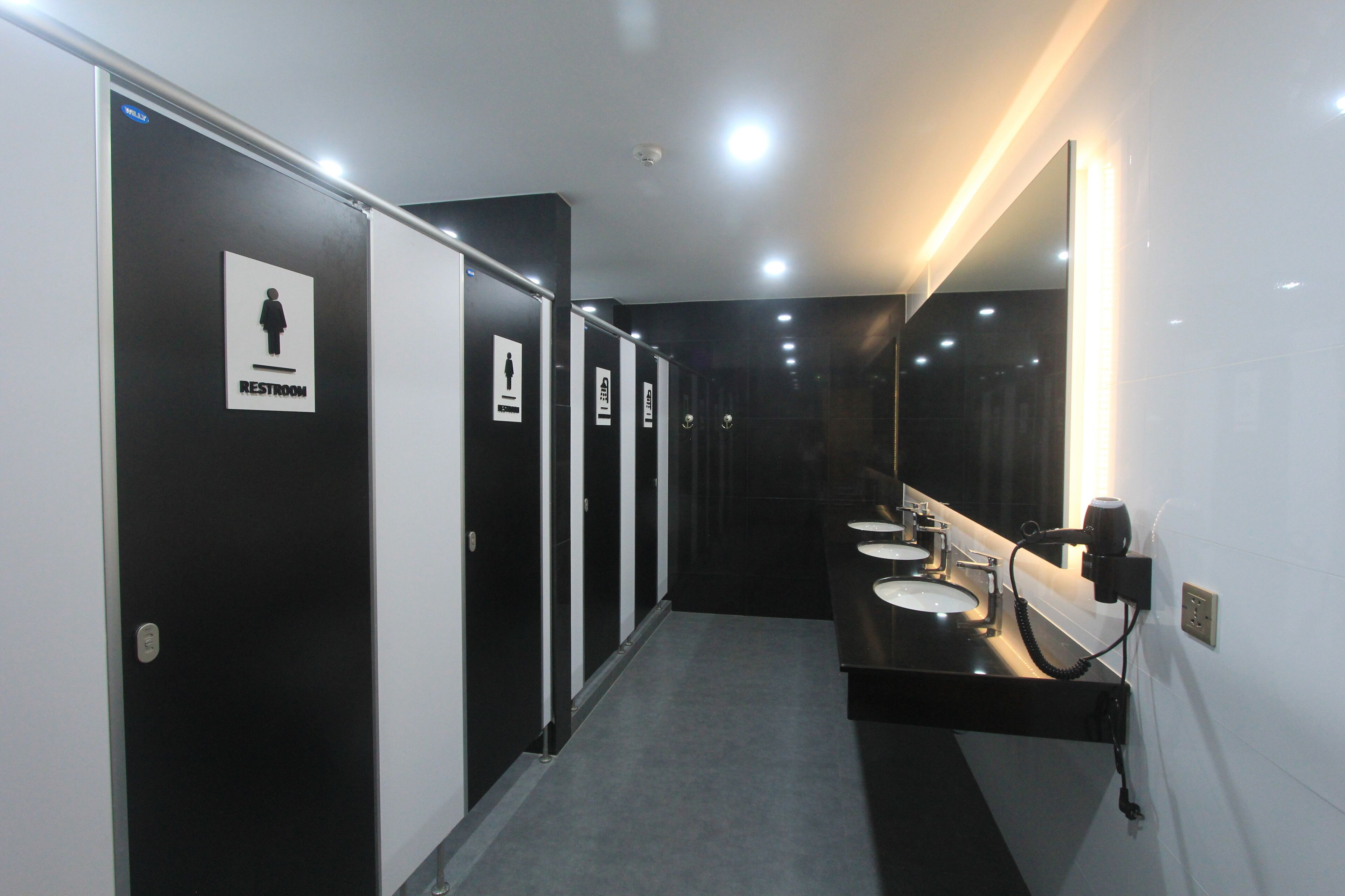 A modern restroom with black and white stalls, a sink, and a mirror.