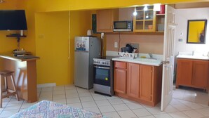Une cuisine compacte équipée d’un réfrigérateur, d’un four à micro-ondes, d’une cuisinière et de meubles de rangement en bois.
