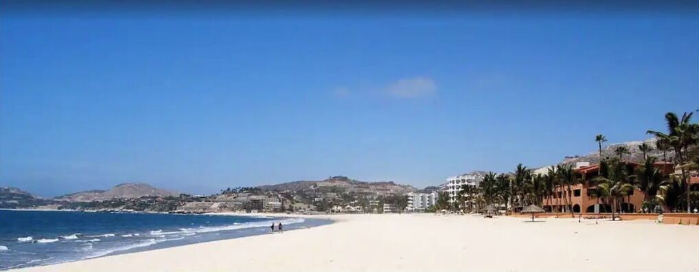A beach with a clear sky, sandy shore, and buildings in the background.